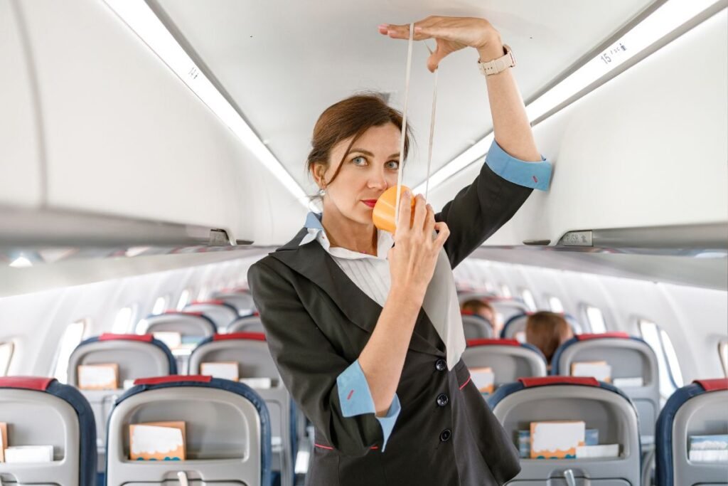 Uma aeromoça demonstrando o uso de uma máscara de oxigênio dentro de um avião, com uma expressão séria e decidida.